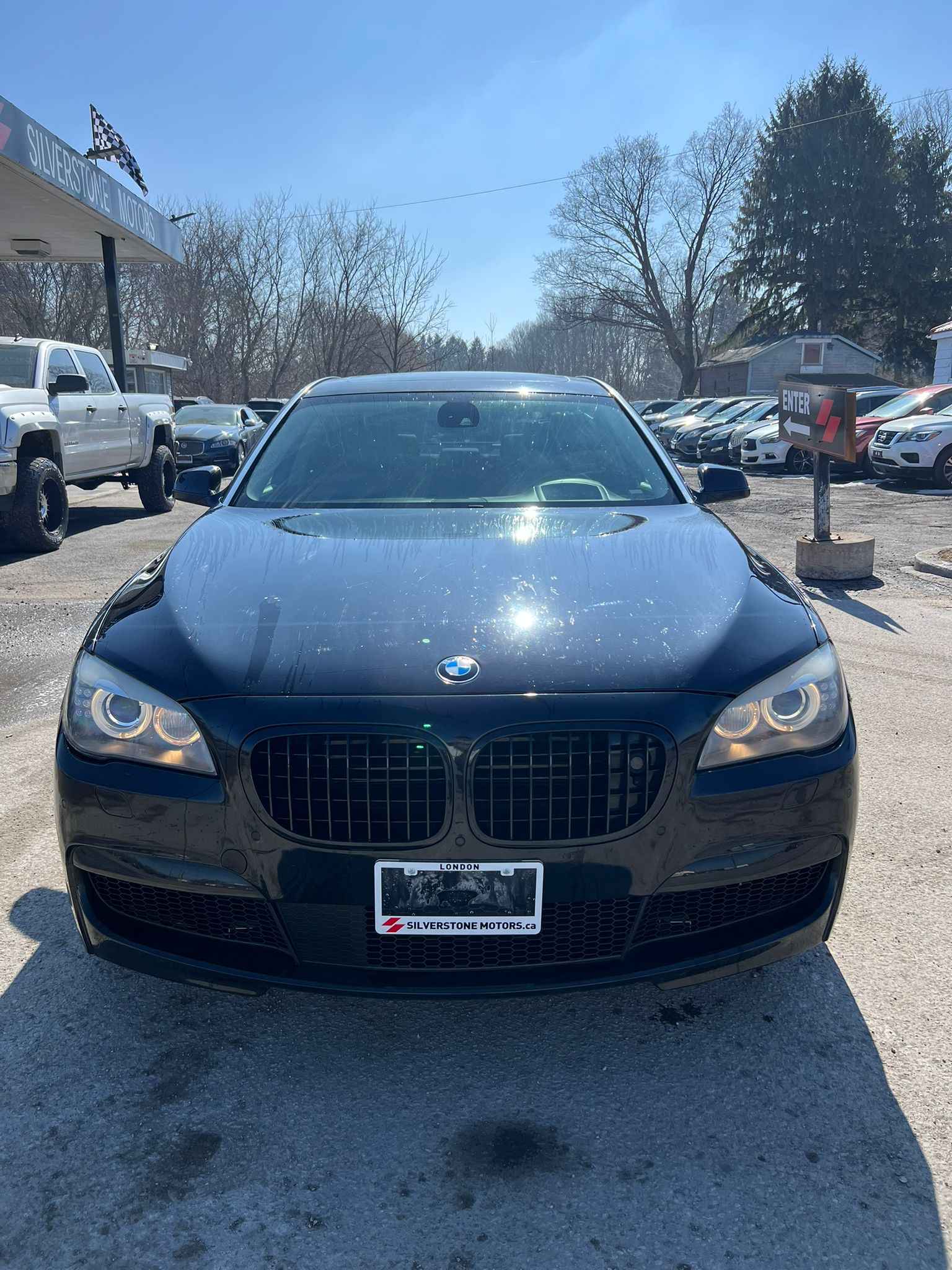 2012 BMW 750LI XDRIVE AWD 4DR BLACK front exterior view at dealership lot with illuminated headlights and distinctive kidney grille.