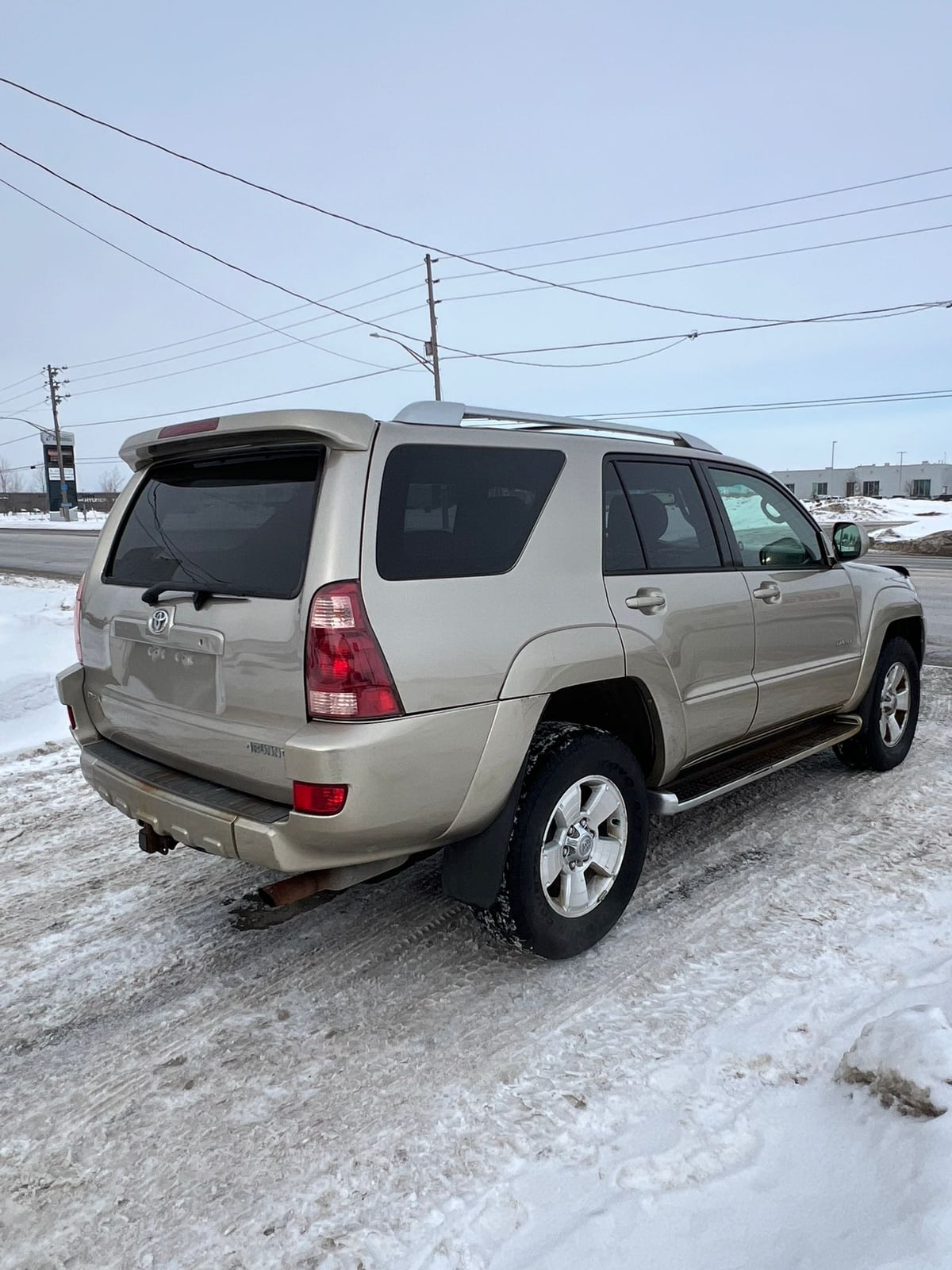 2003 Toyota 4RUNNER LIMITED V8 4WD Gold rear three-quarter exterior view showing taillights and alloy wheels in snowy parking lot.