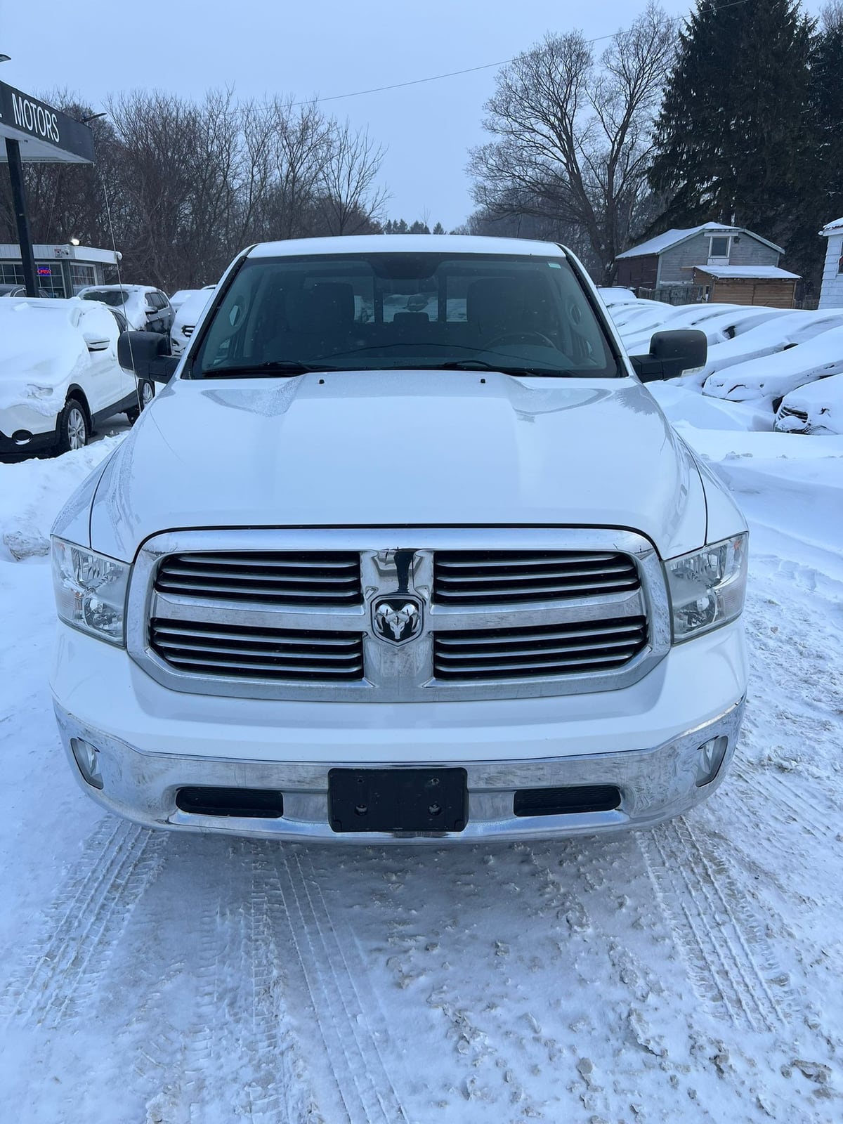 2013 RAM 1500 SLT CREW CAB 4WD SHORT BOX 140.5″ White front exterior view in snowy dealership lot with distinctive RAM grille badging.
