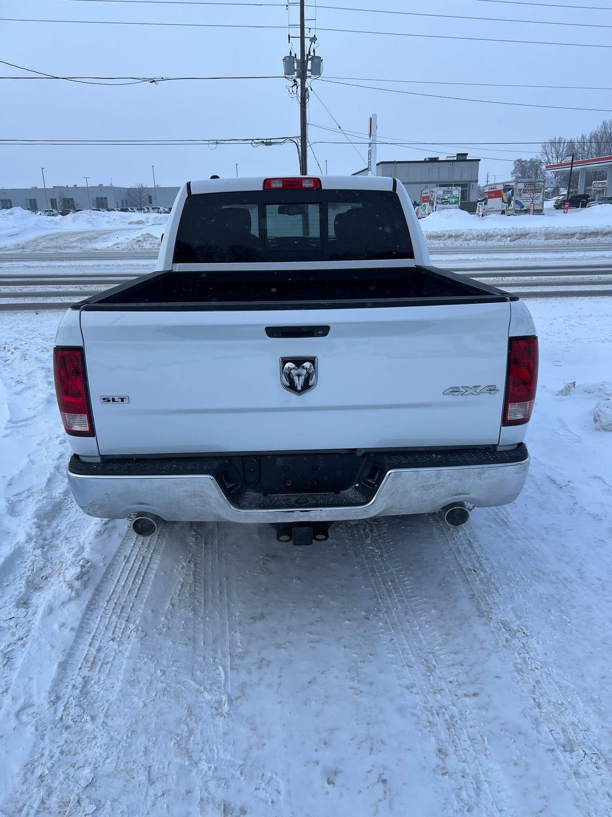 2013 RAM 1500 SLT CREW CAB 4WD SHORT BOX 140.5″ White rear exterior view showing bed cover, badging, and tailgate in snowy lot.