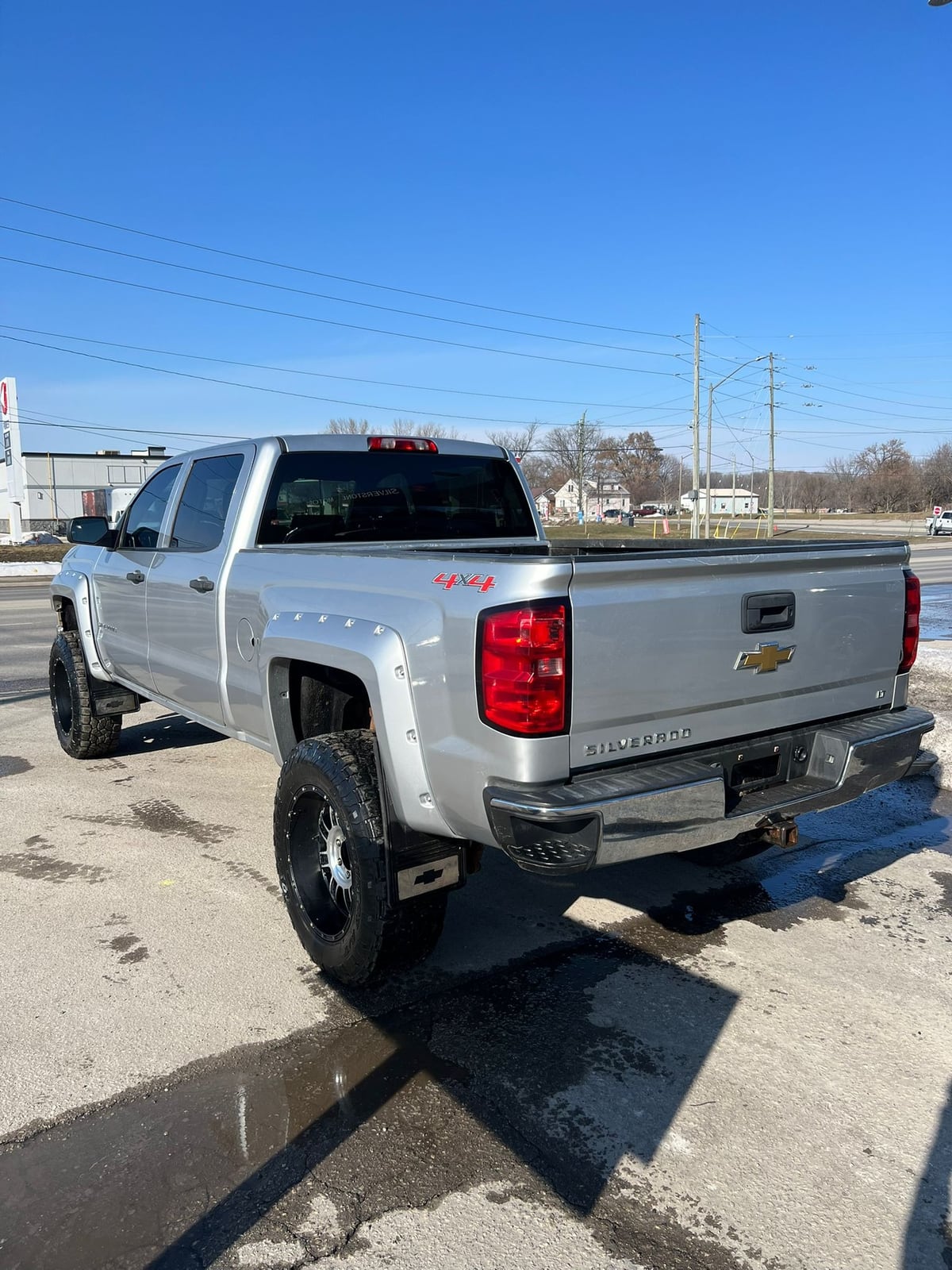 2014 Chevrolet SILVERADO 1500 LT w/1LT 4WD CREWCAB SILVER rear three-quarter exterior view with 4x4 badging and custom wheels in daylight.