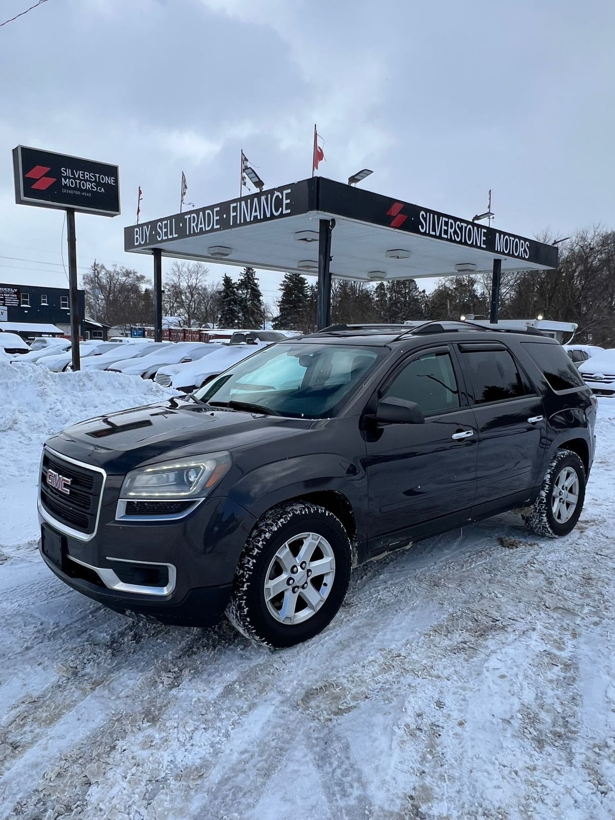 2015 GMC ACADIA SLE AWD 4DR GRAY front three-quarter exterior view with chrome accents and alloy wheels at snowy dealership lot.