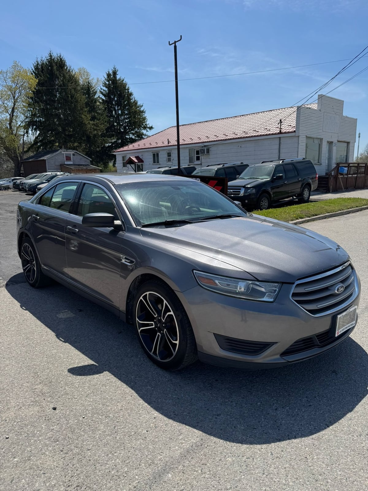 2014 Ford TAURUS SE FWD 4DR GRAY front three-quarter exterior view with distinctive multi-spoke alloy wheels in dealership lot.