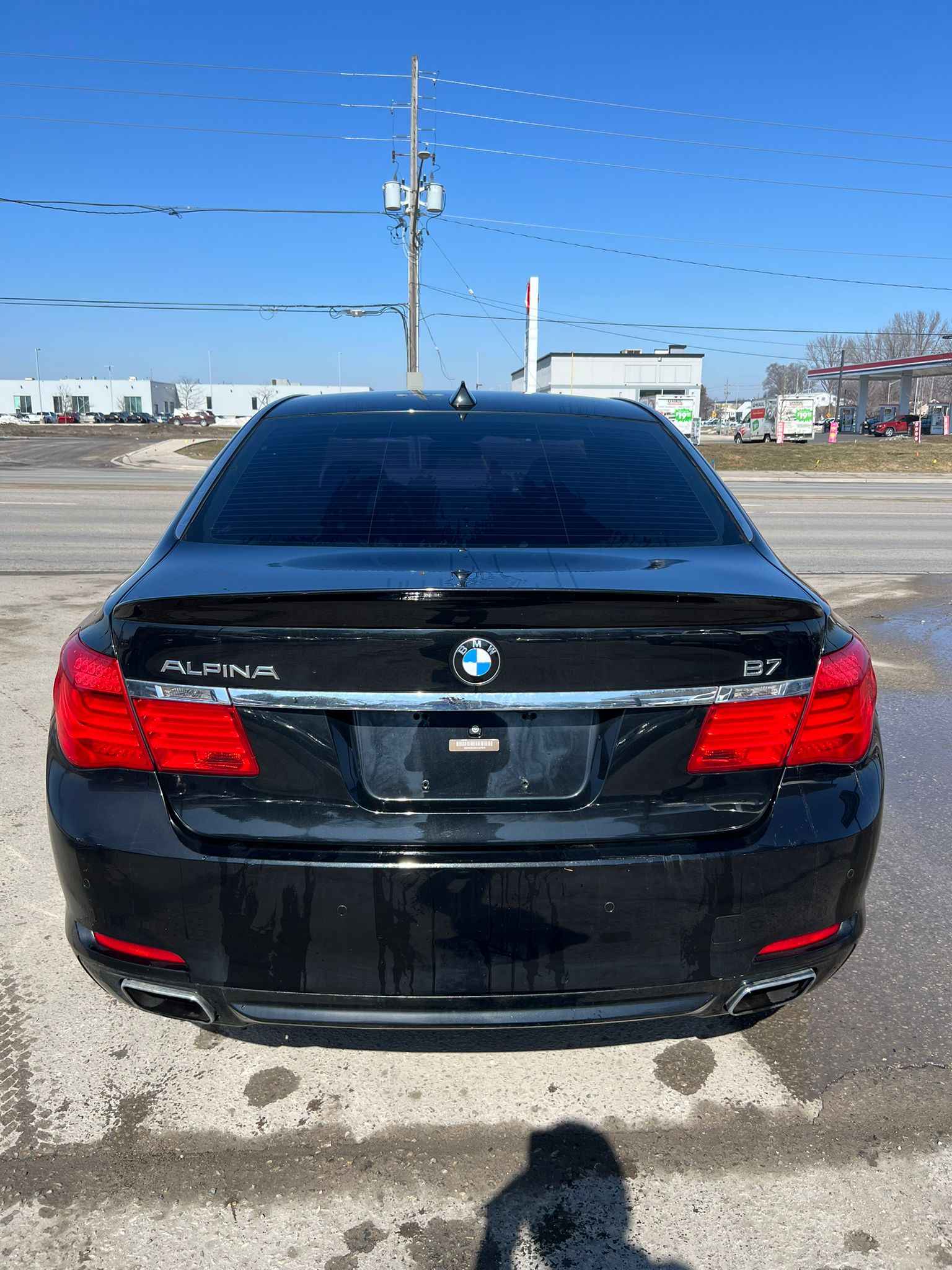 2012 BMW 750LI XDRIVE AWD 4DR BLACK rear exterior view showing trunk lid, red taillights, and chrome badging in parking lot.
