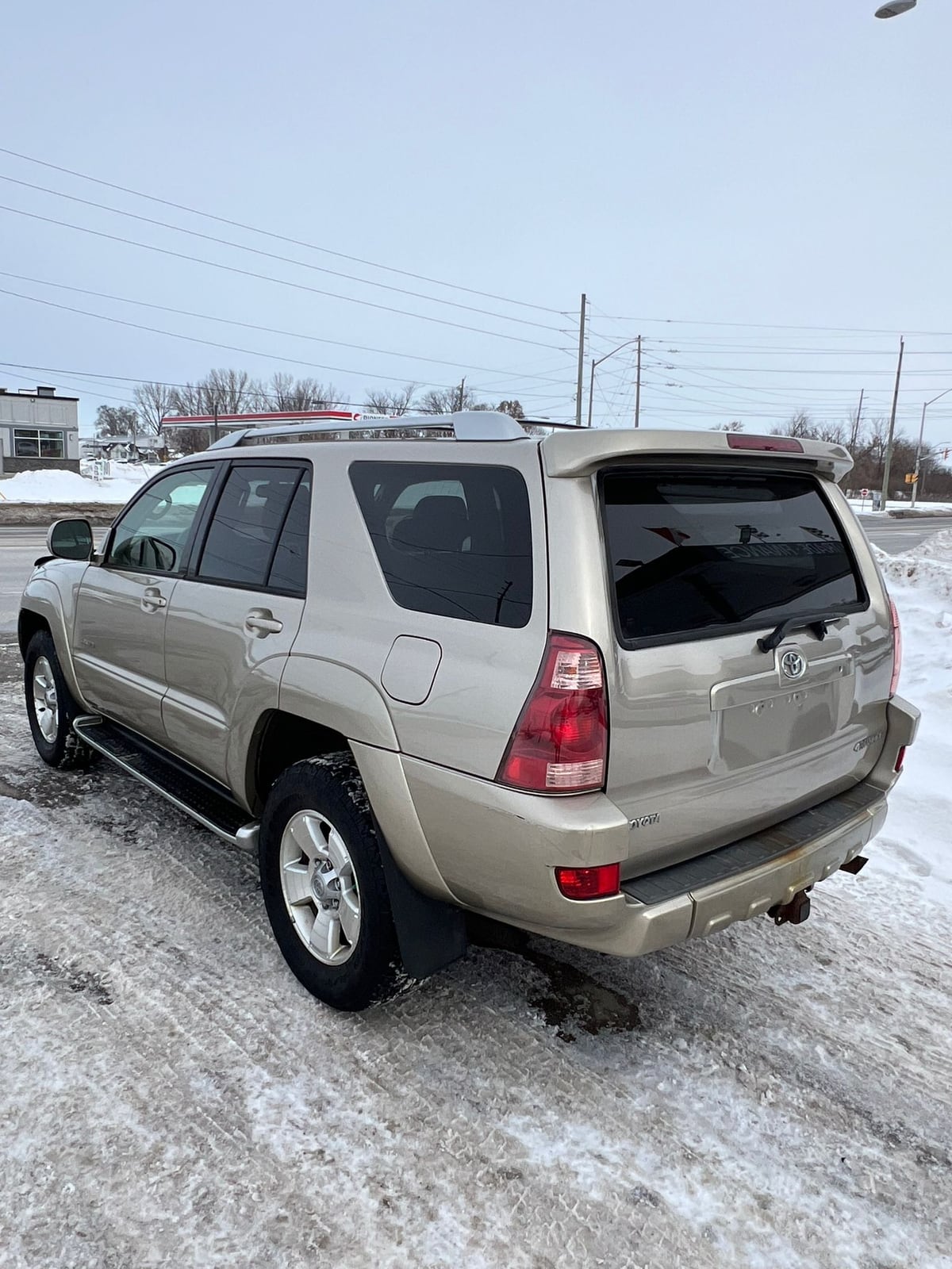 2003 Toyota 4RUNNER LIMITED V8 4WD Gold rear three-quarter exterior view with alloy wheels and roof rack in snowy lot.