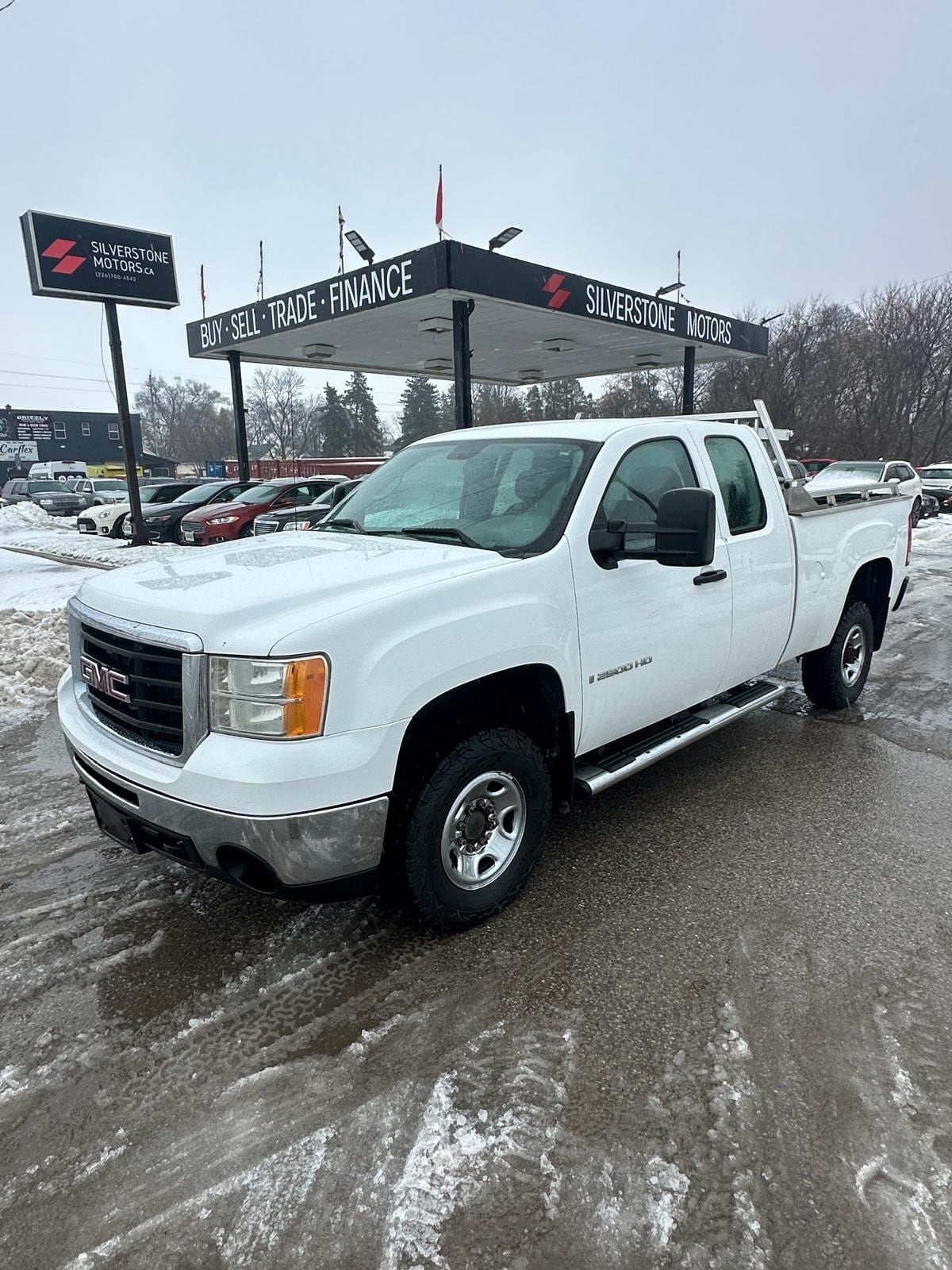 2007 GMC 2500HD DURAMAX DIESEL SIERRA 2500HD 6.6 DURAMAX DIESEL WT EXTENDED CAB STD White front three-quarter exterior view at dealership lot with chrome wheels visible.