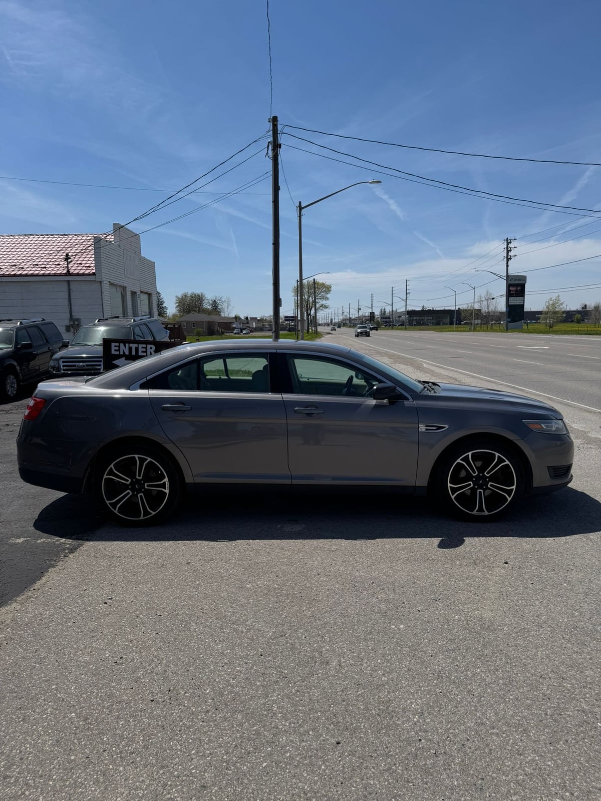 2014 Ford TAURUS SE FWD 4DR GRAY driver side exterior view with alloy wheels in dealership lot.