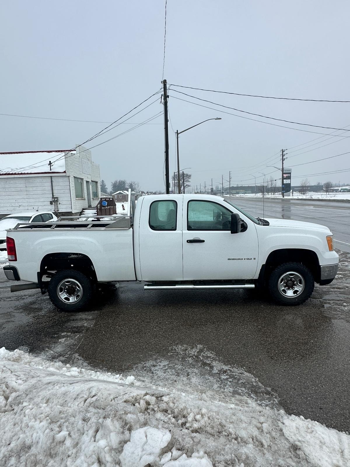 2007 GMC 2500HD DURAMAX DIESEL SIERRA 2500HD 6.6 DURMAX DIESEL WT EXTENDED CAB STD White side exterior view with chrome wheels in winter lot setting.