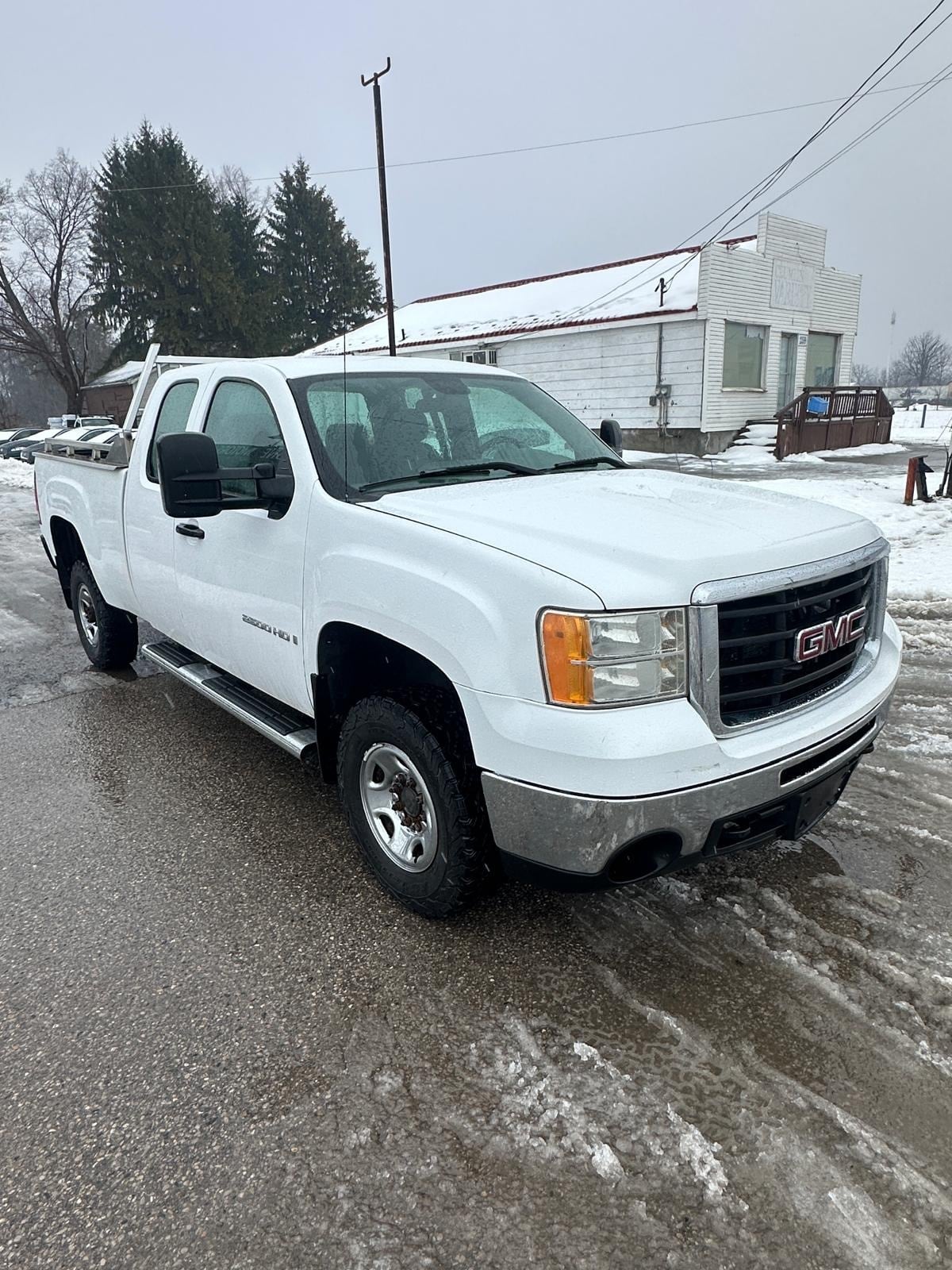 2007 GMC 2500HD DURAMAX DIESEL SIERRA 2500HD 6.6 DURMAX DIESEL WT EXTENDED CAB STD White front three-quarter exterior view with chrome grille and wheels in snowy winter setting.