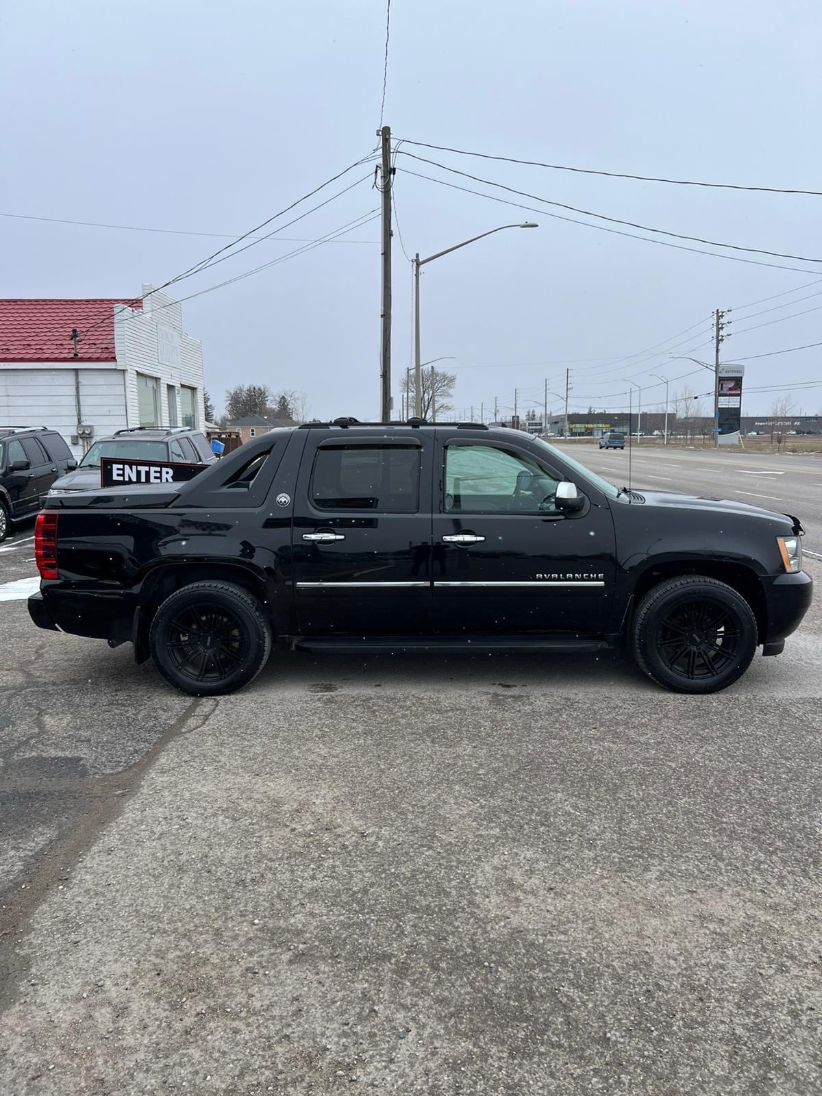 2013 Chevrolet Avalanche LTZ BLACK DIAMOND EDITION 4WD 4DR BLACK shown in left side exterior view with black alloy wheels in dealership lot.
