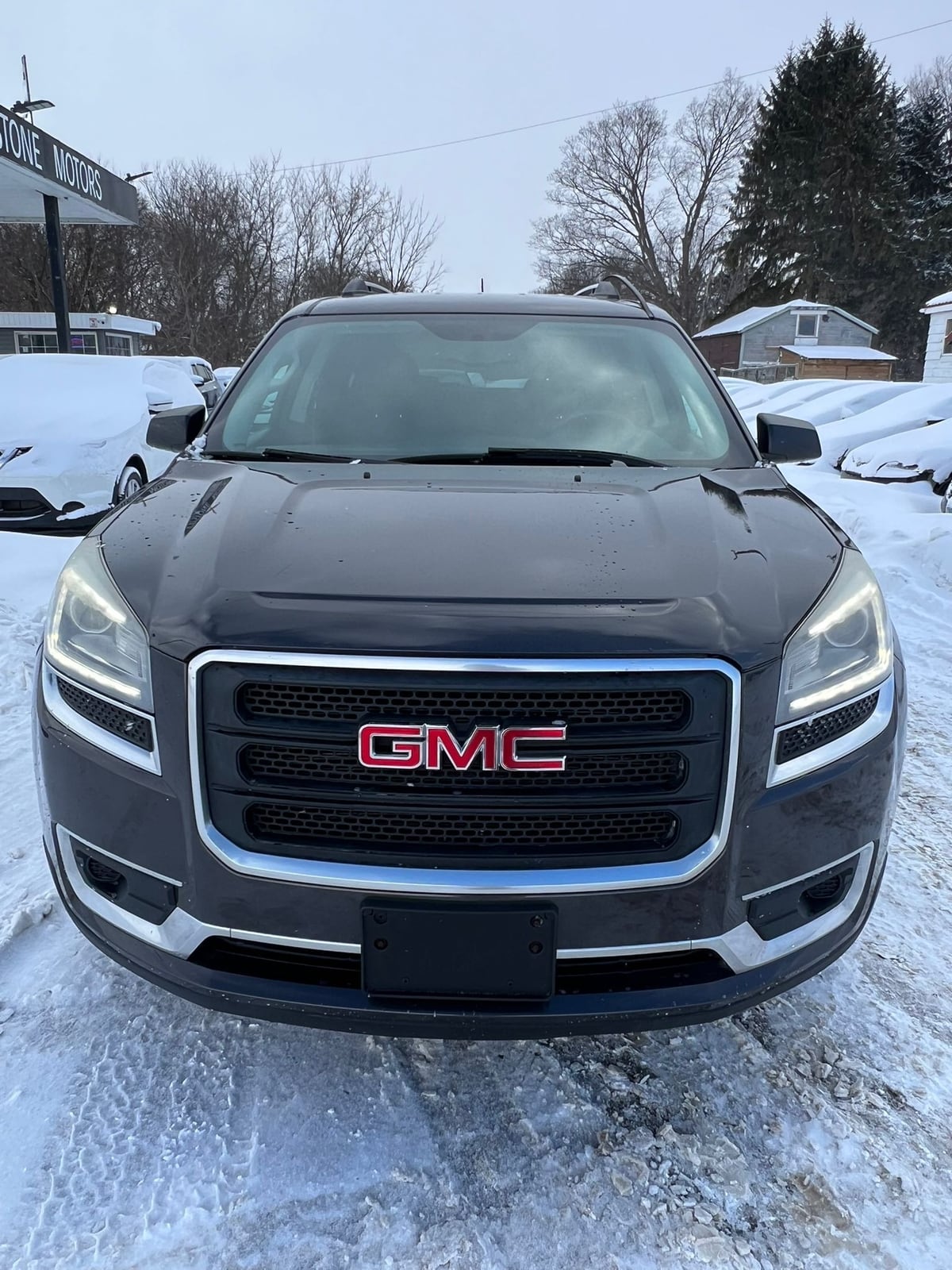 2015 GMC ACADIA SLE AWD 4DR GRAY front exterior view with LED headlights and chrome grille trim in snowy dealership lot.