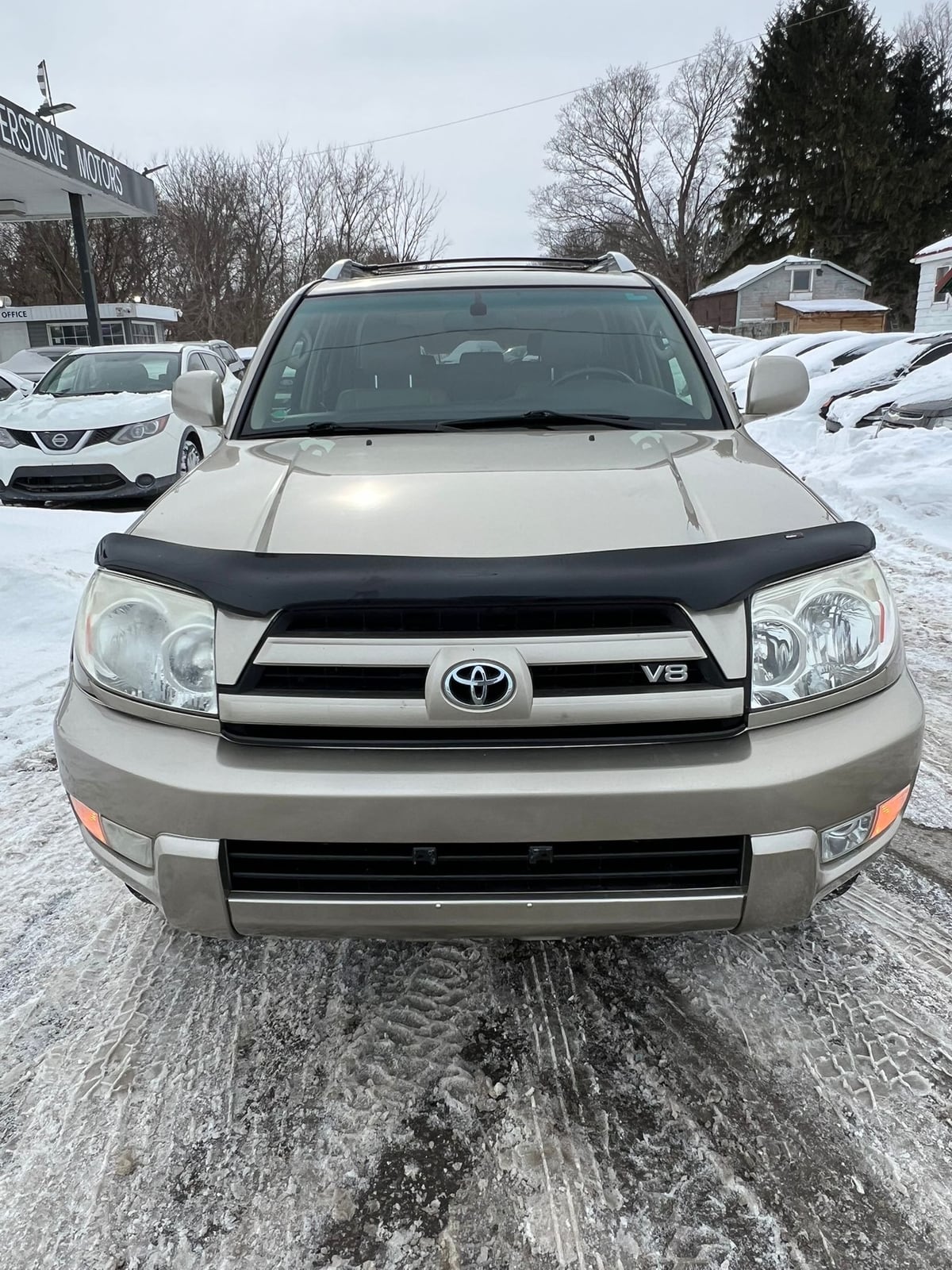2003 Toyota 4RUNNER LIMITED V8 4WD Gold front exterior view with black grille and hood deflector, parked in snowy dealership lot.