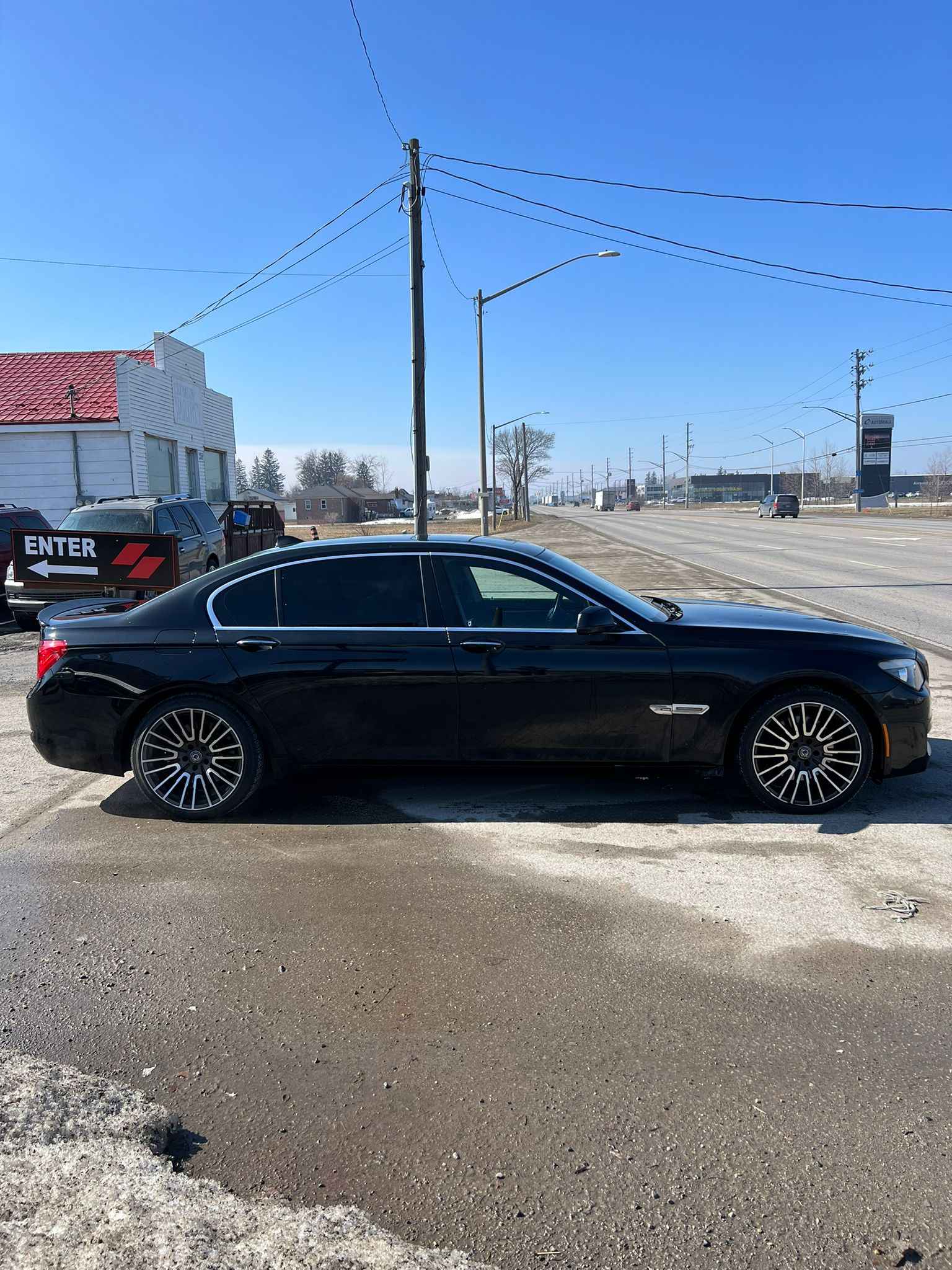 2012 BMW 750LI XDRIVE AWD 4DR BLACK side profile exterior view with multi-spoke alloy wheels in commercial lot setting.